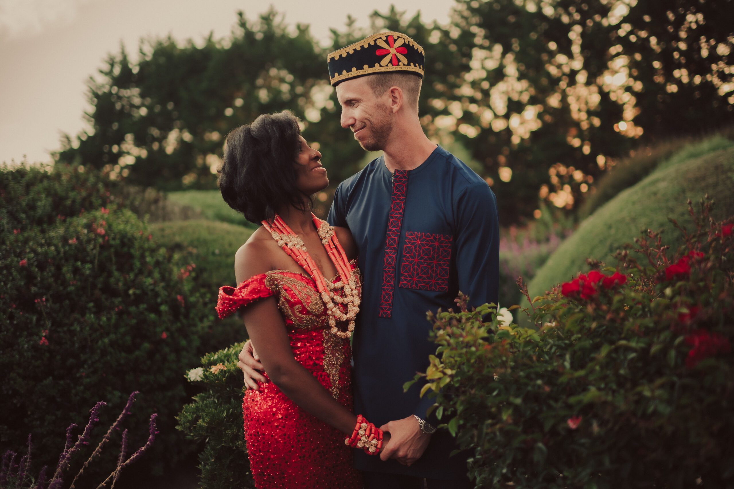 Tracy and Alex holding hands in richly embroidered wedding attire among the gardens at Heritage Estates
