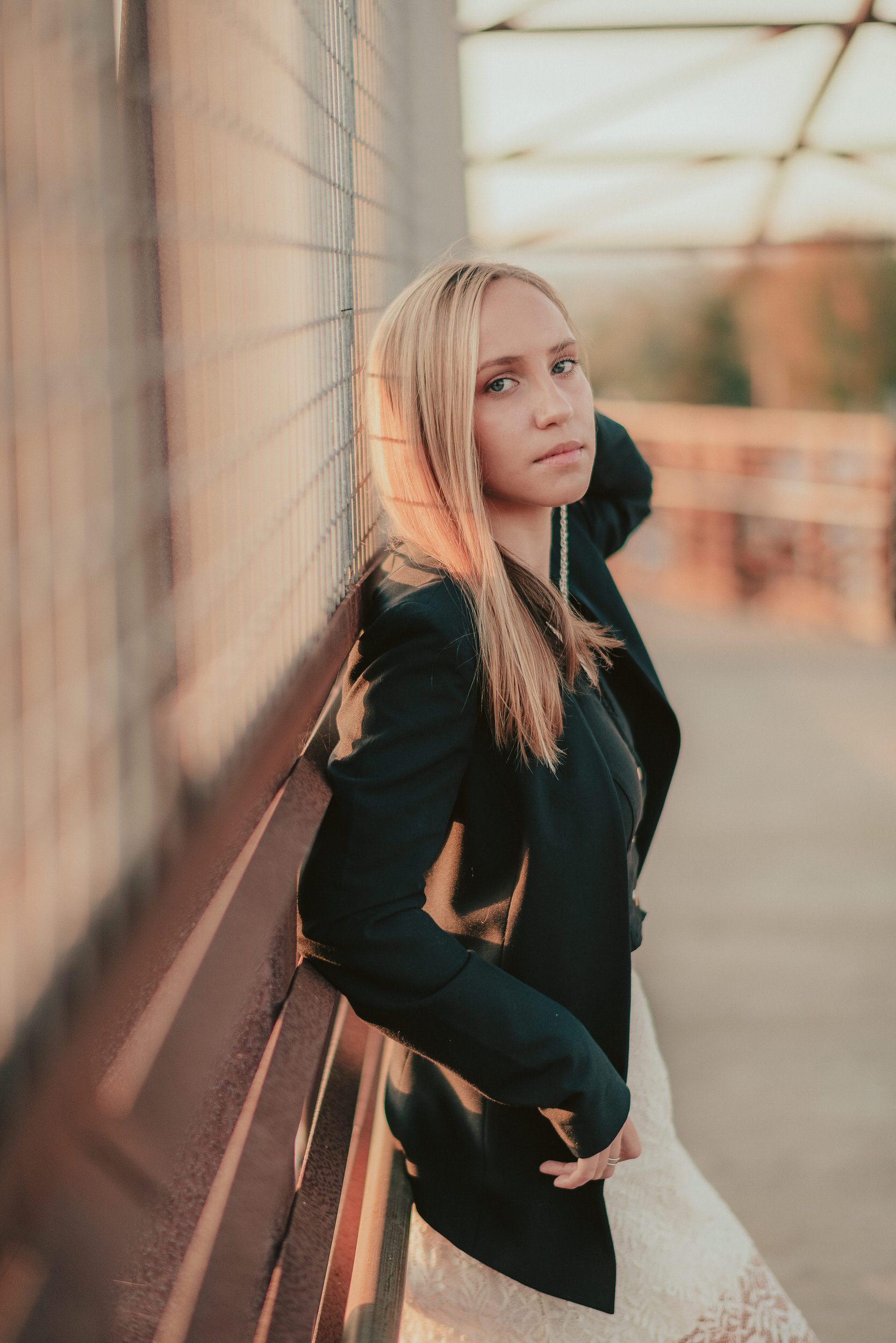 Warm backlit senior portrait beside an urban fence