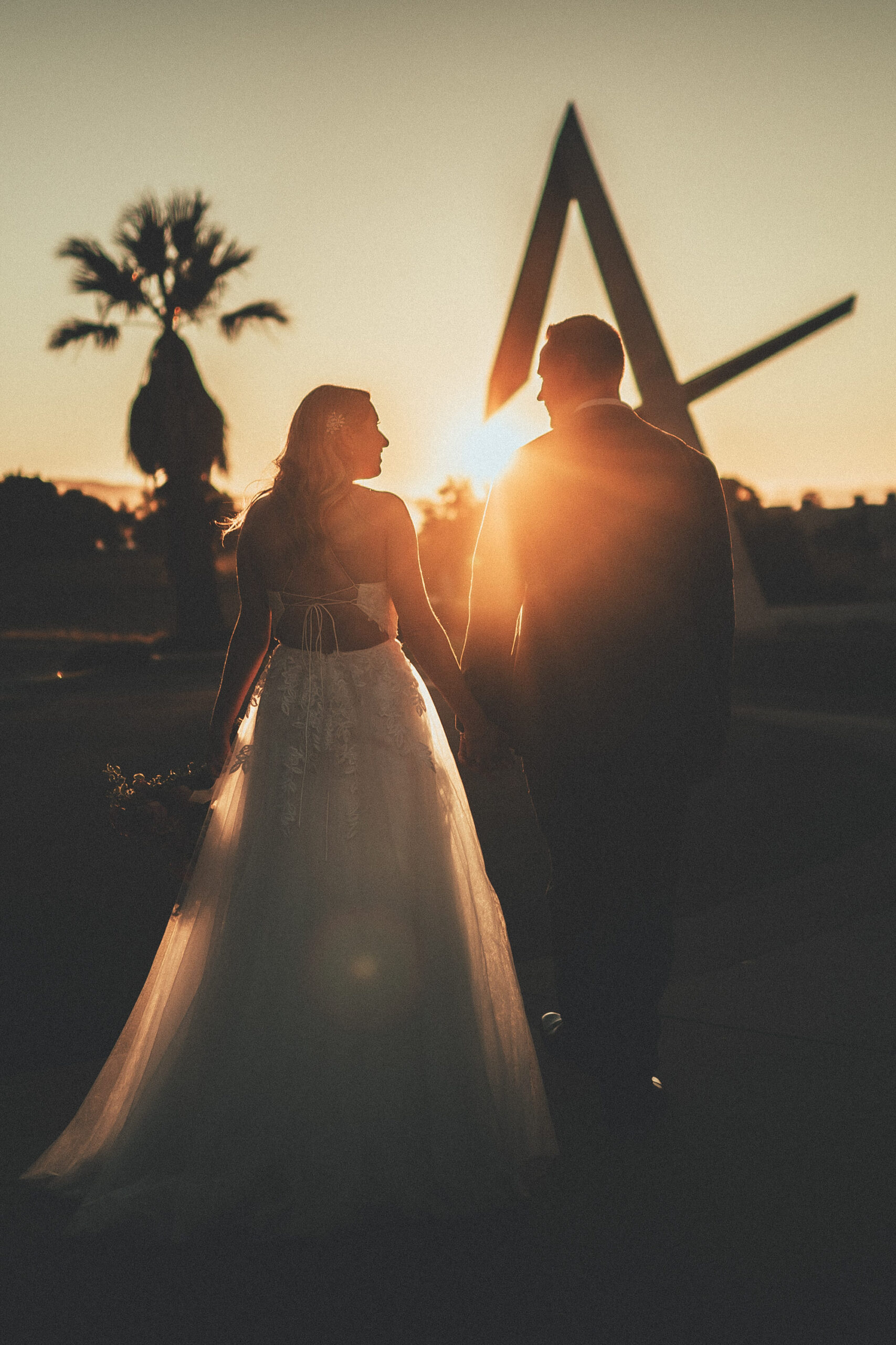 Claire and Tony holding hands at sunset beneath the sculptural arch at SLO Brew Rock
