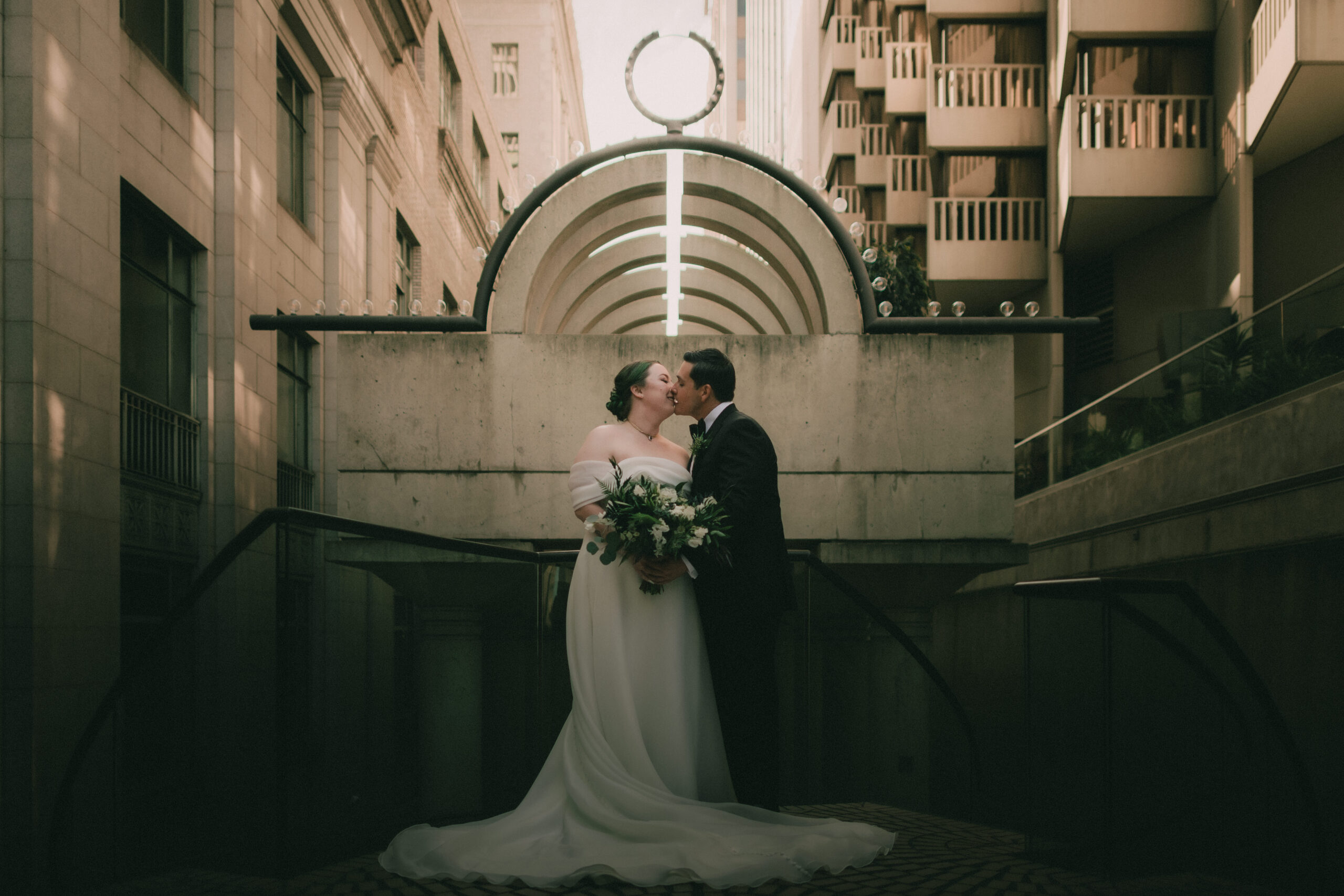 Anne and Charles kiss beneath a moody geometric downtown backdrop