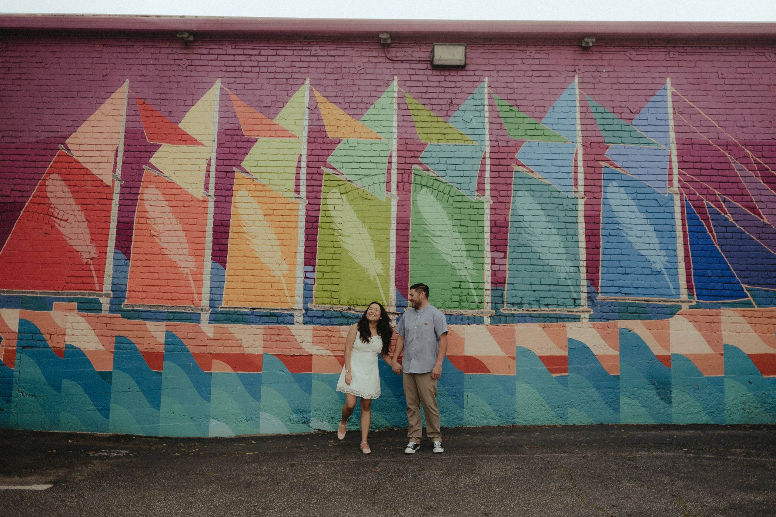 Ashley and Adam holding hands in front of a colorful downtown San Luis Obispo mural