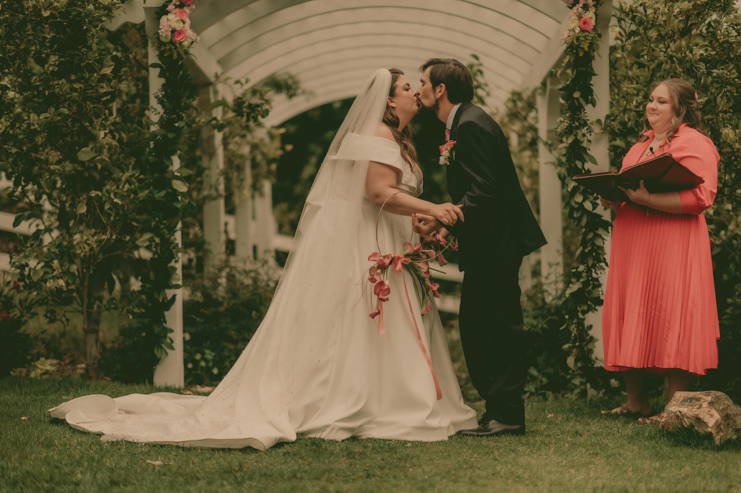 Calla and Bryan kiss beneath a flower-covered garden arch