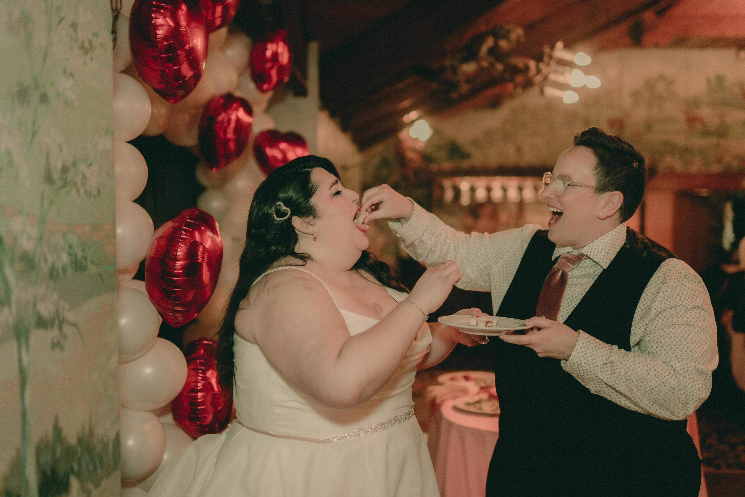 Shaye and Elizabeth playfully feed one another cake at their reception
