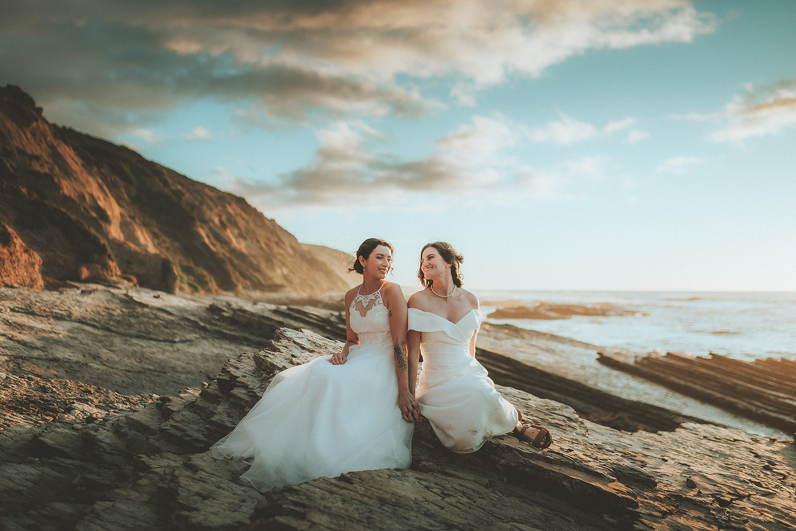 Two brides in a wide cinematic portrait on the Montaña de Oro coastline