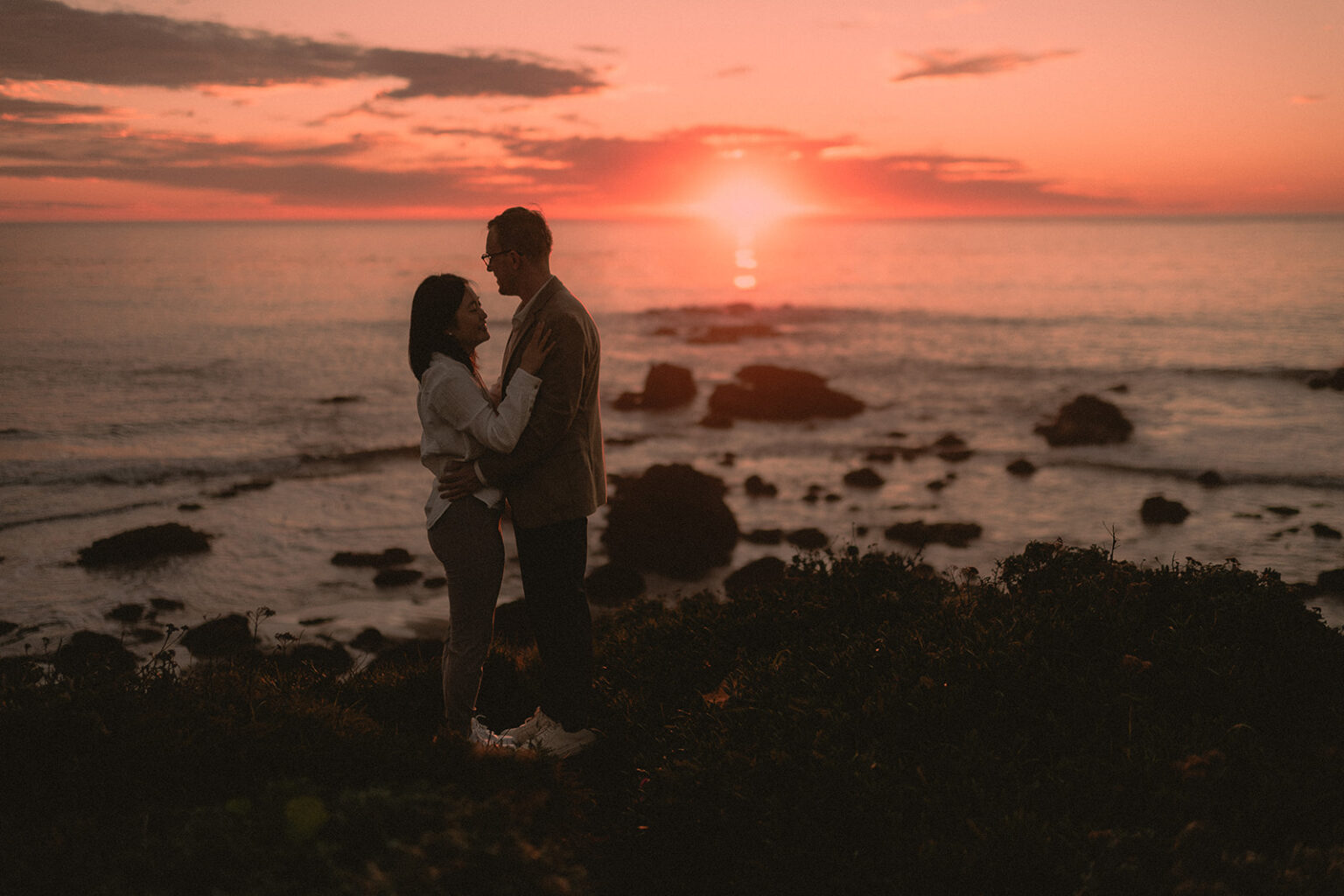 Newly engaged couple silhouetted against a coastal sunset