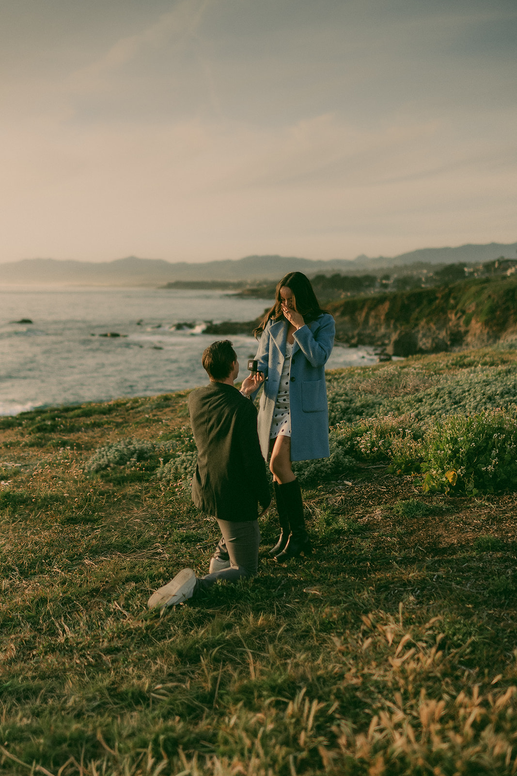 One partner kneeling during a surprise proposal on the coast