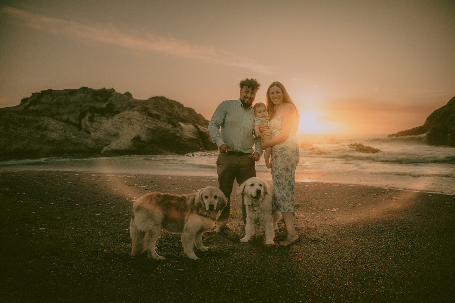 Family with a baby and dogs at the shoreline during golden hour