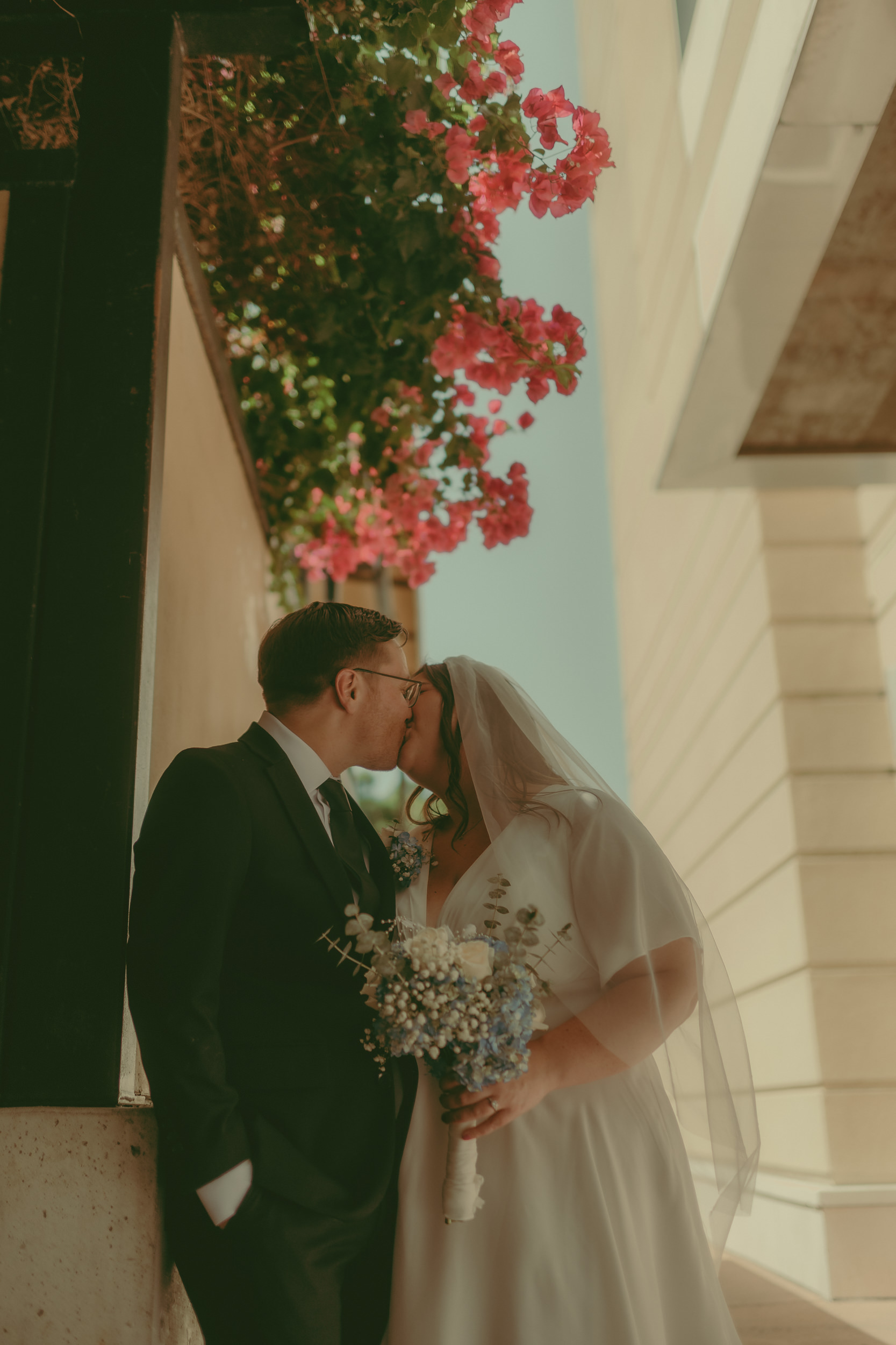 Tiffani and Braden kiss beside flowers and downtown architecture.