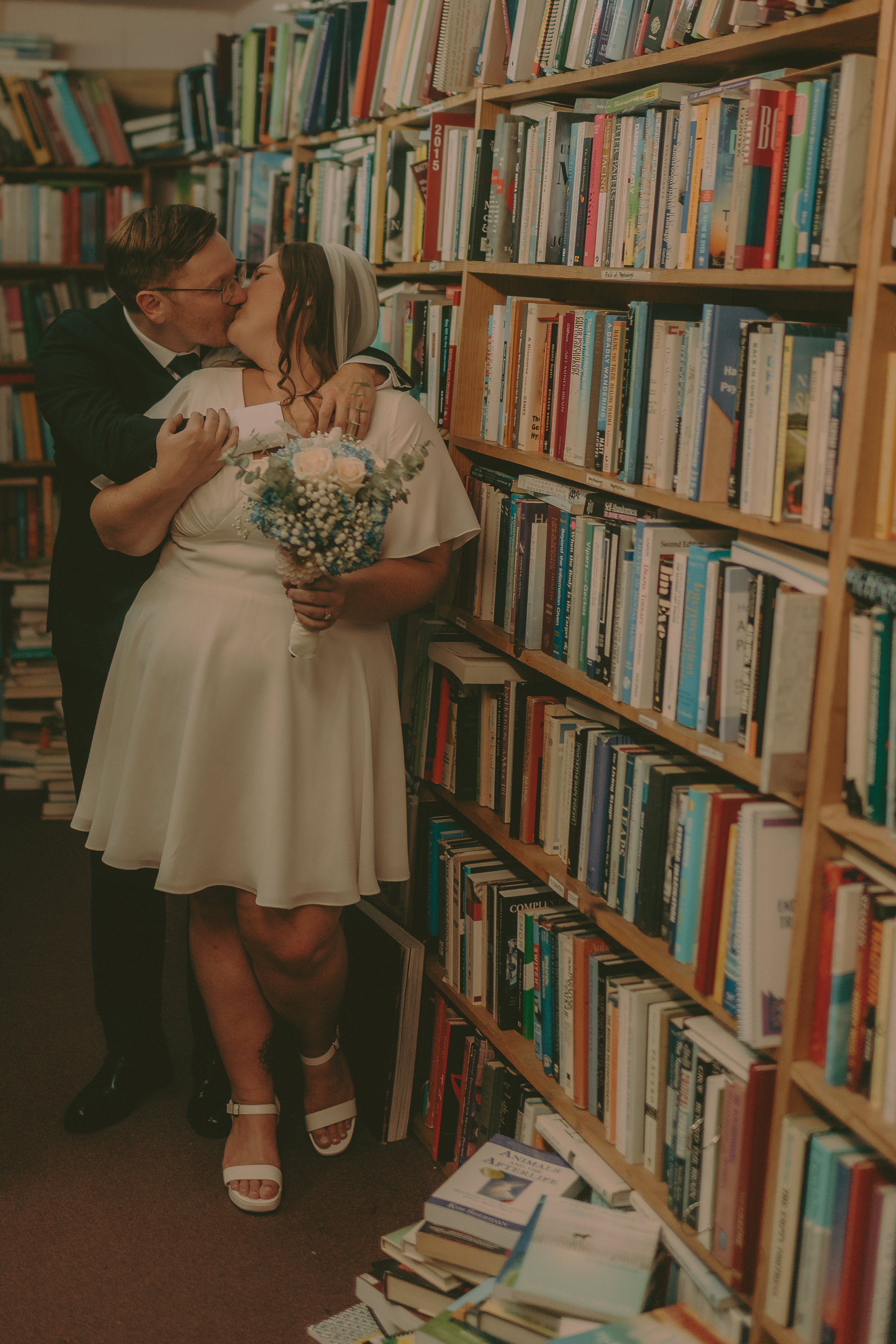 Tiffani and Braden kiss in a narrow bookstore aisle.