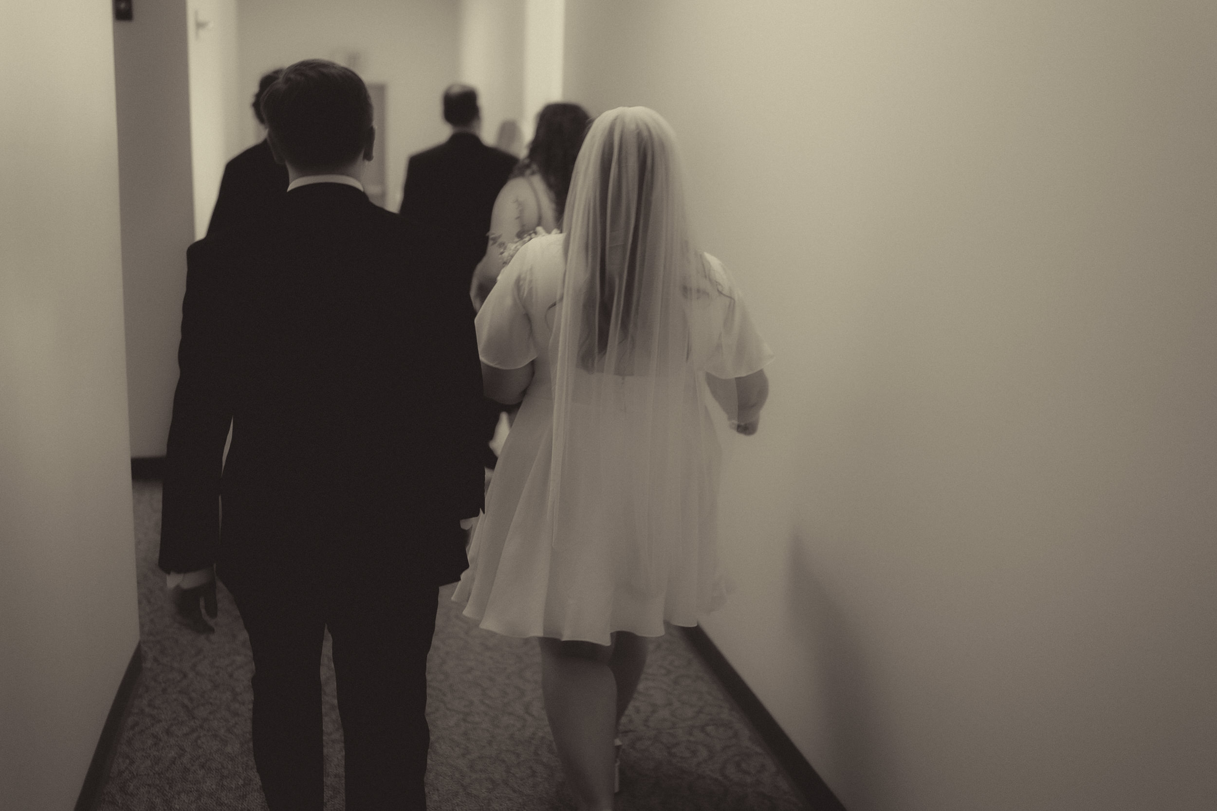 Tiffani and Braden walk through a courthouse hallway in a black-and-white photograph.