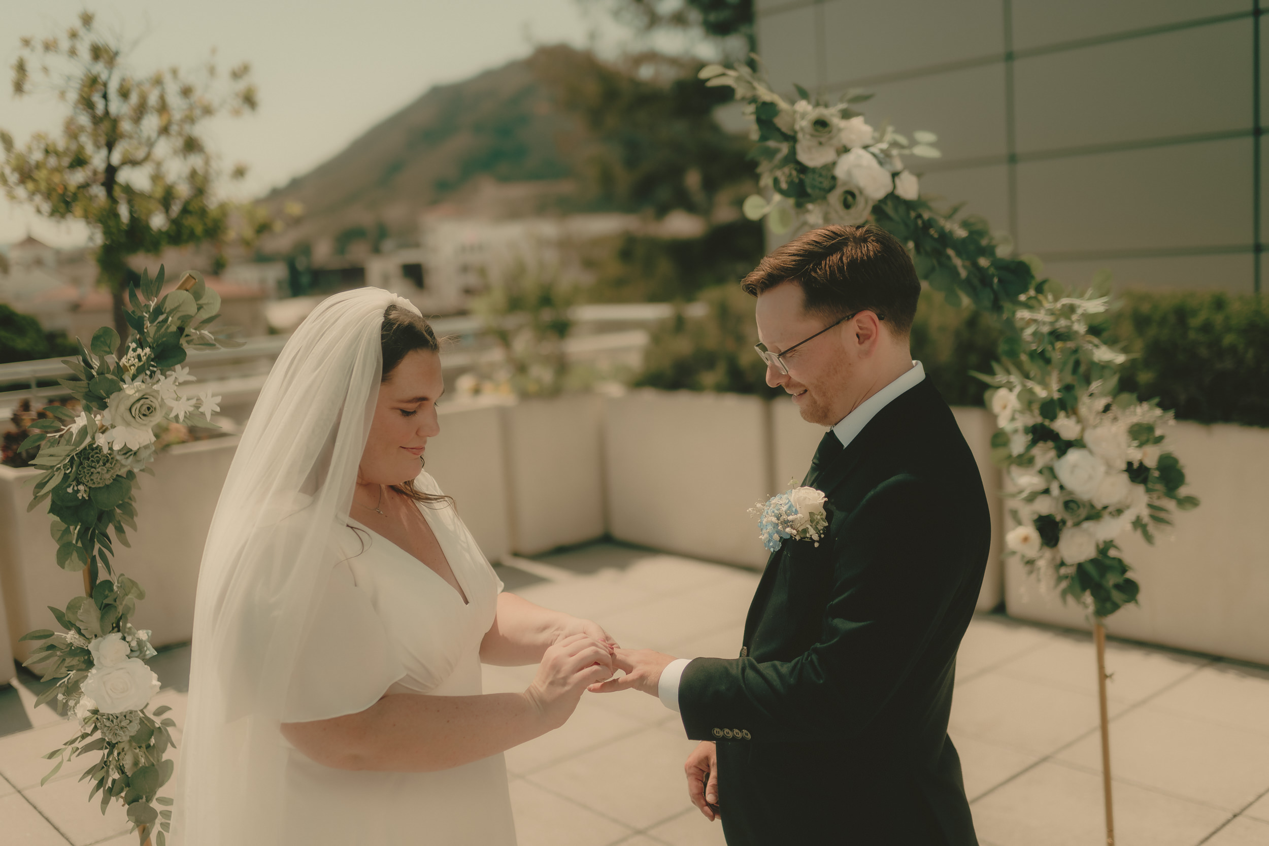Tiffani and Braden exchange rings beneath the rooftop floral arch.