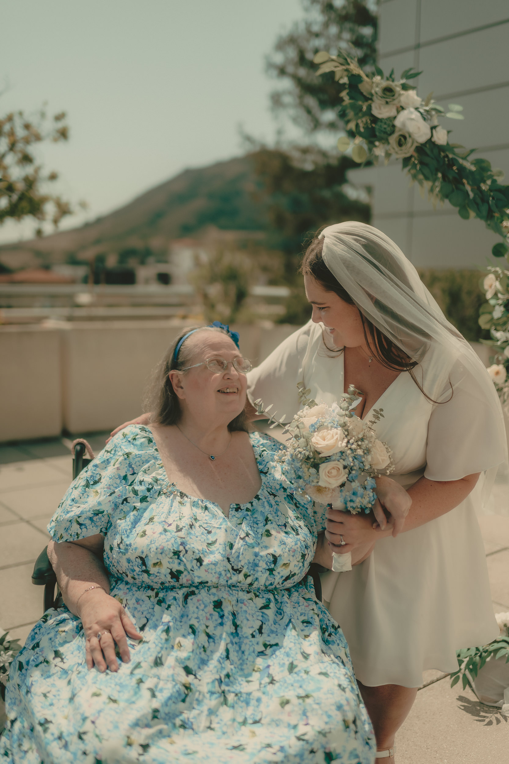Tiffani leans close to a smiling guest in a blue floral dress after the ceremony.