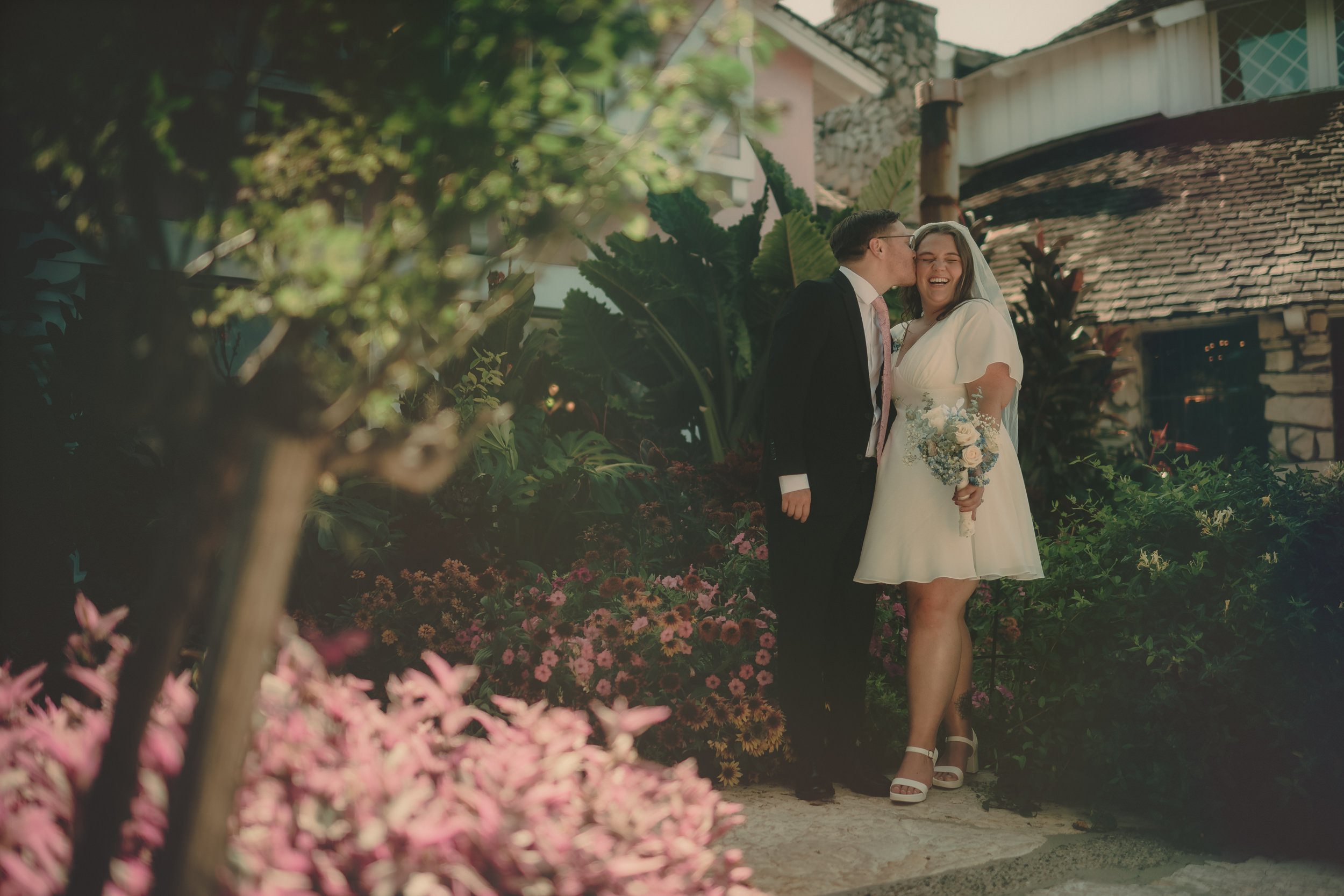 Braden kisses Tiffani's cheek in a wide garden portrait at Madonna Inn.