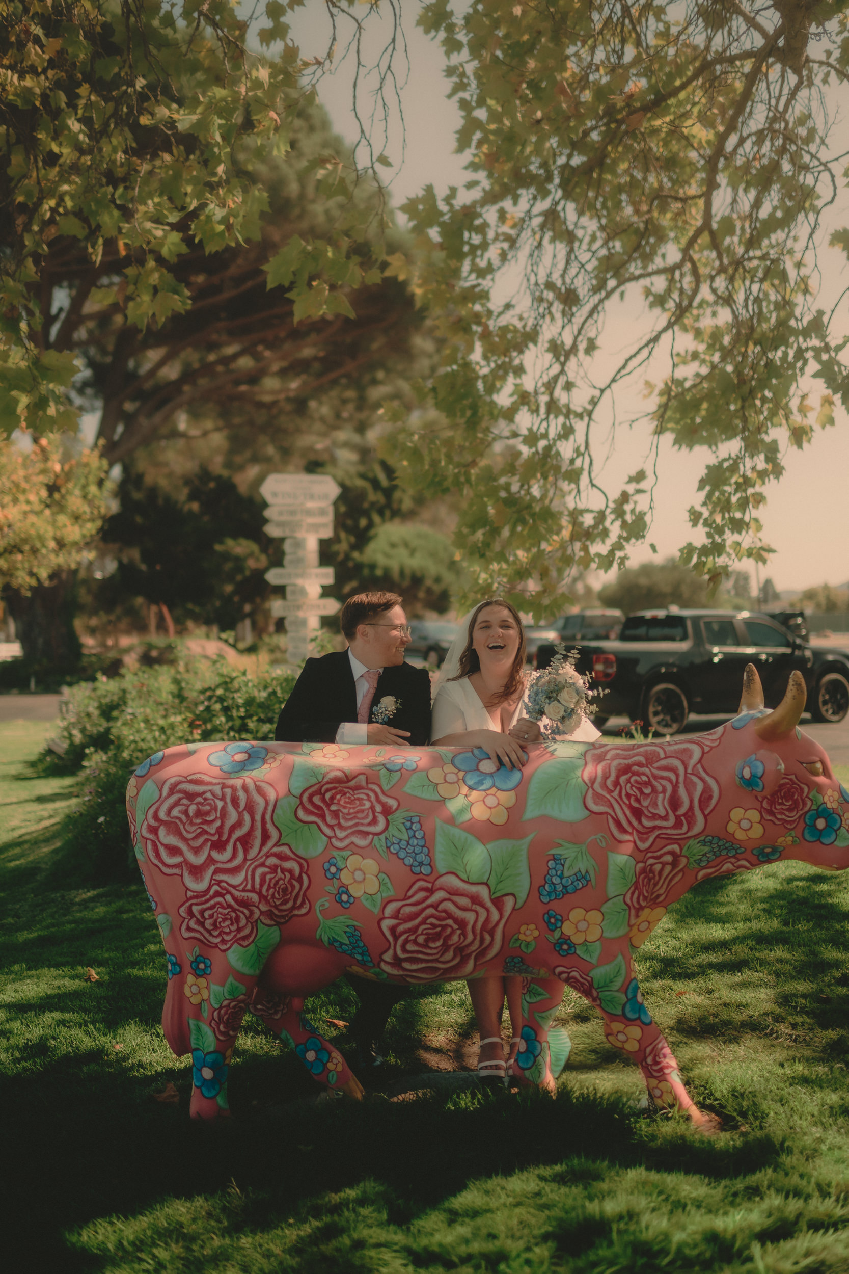 Tiffani and Braden laugh behind the Madonna Inn floral cow.