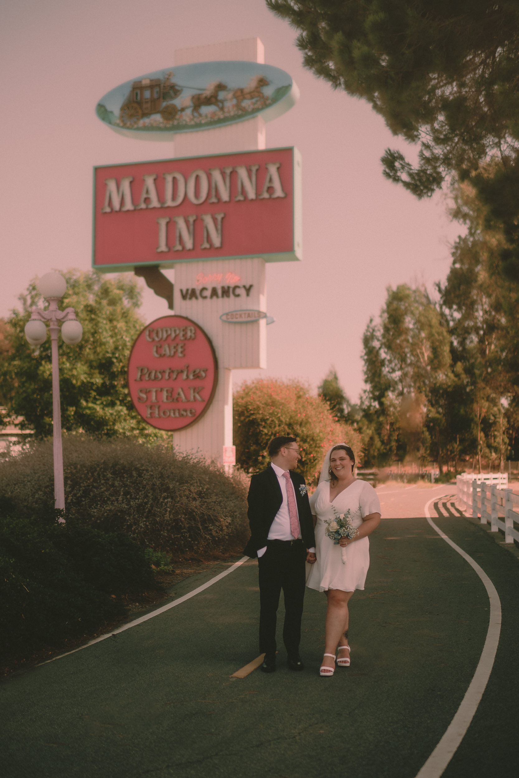 The vintage Madonna Inn roadside sign glows in soft pink afternoon light.