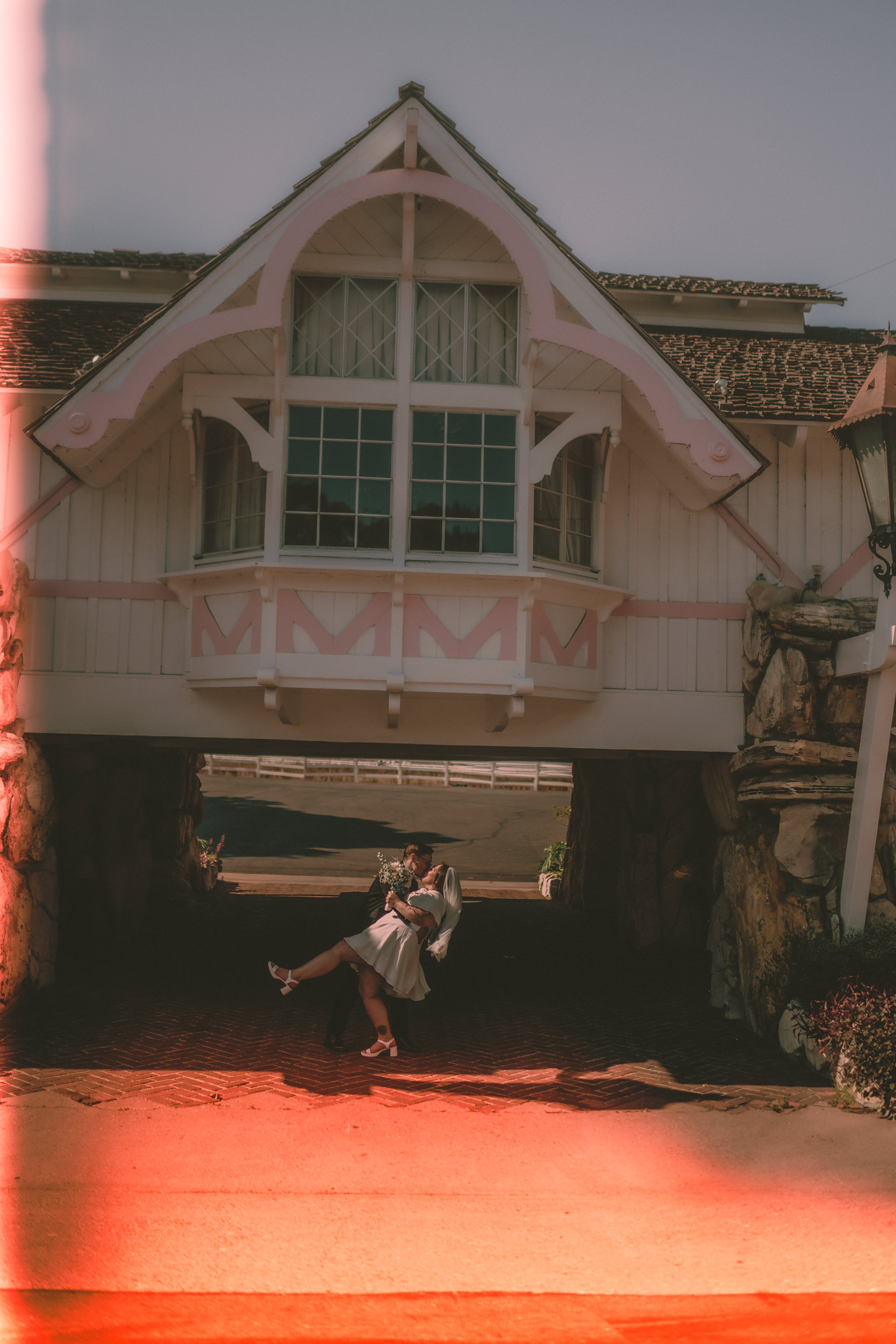 Tiffani and Braden dip beneath the Madonna Inn entrance while a red light leak fills the frame.