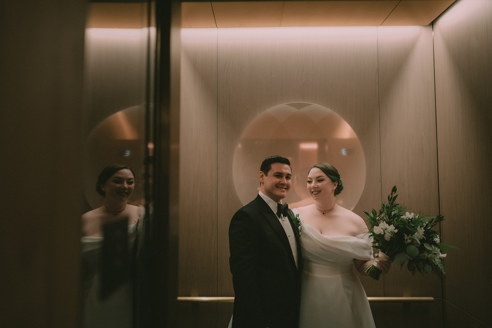 Anne and Charles reflected in the warm wood paneling of a San Francisco elevator.