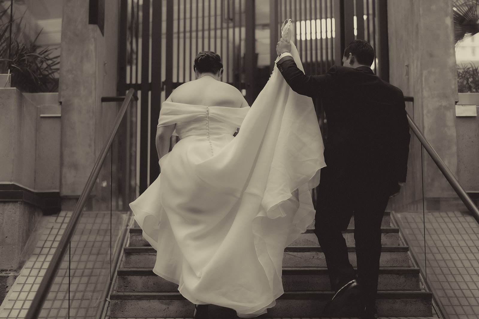 Black-and-white view of Anne and Charles walking up an outdoor staircase framed by tall city columns.