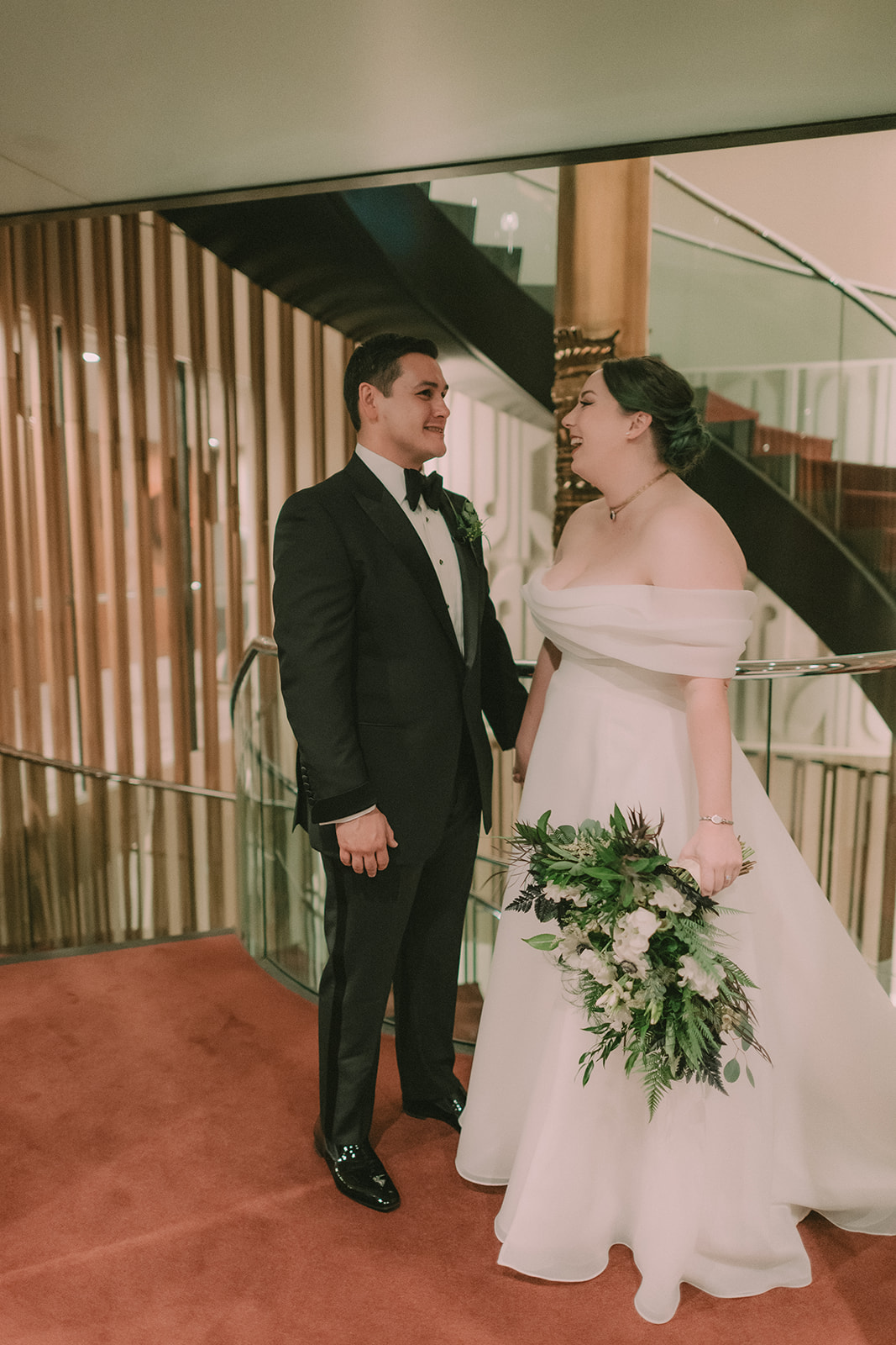 Anne and Charles laugh together beside a curved staircase at The Jay Hotel.