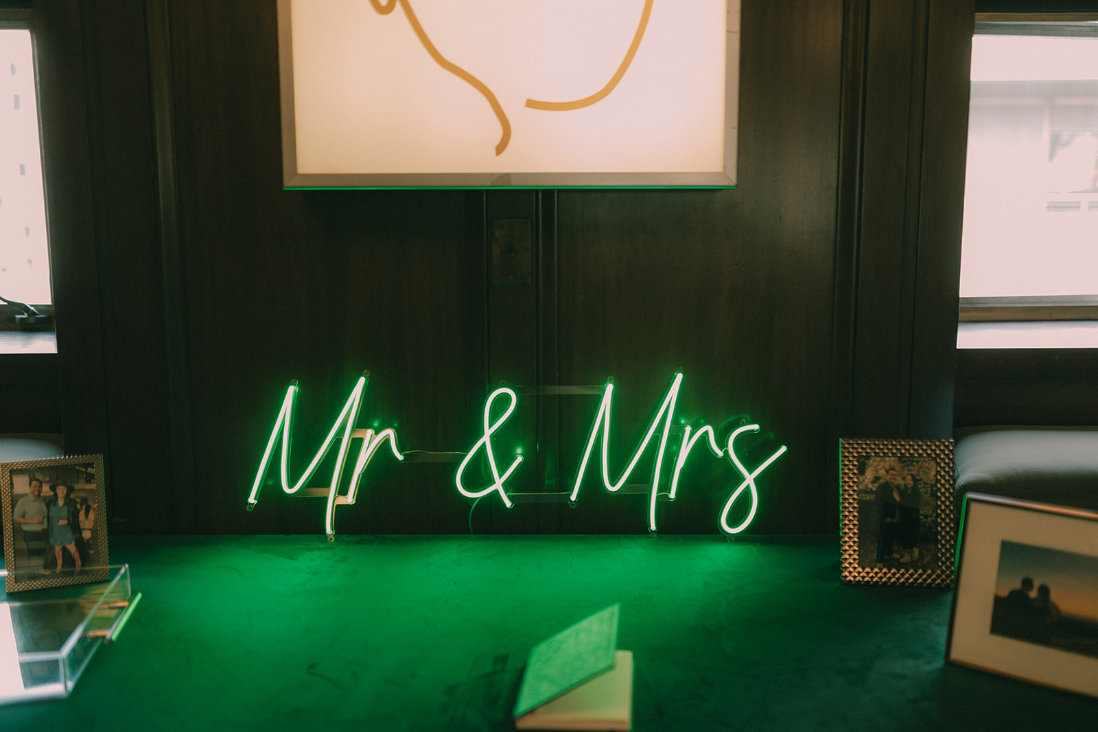 Green neon Mr and Mrs sign surrounded by framed photographs and wedding keepsakes.