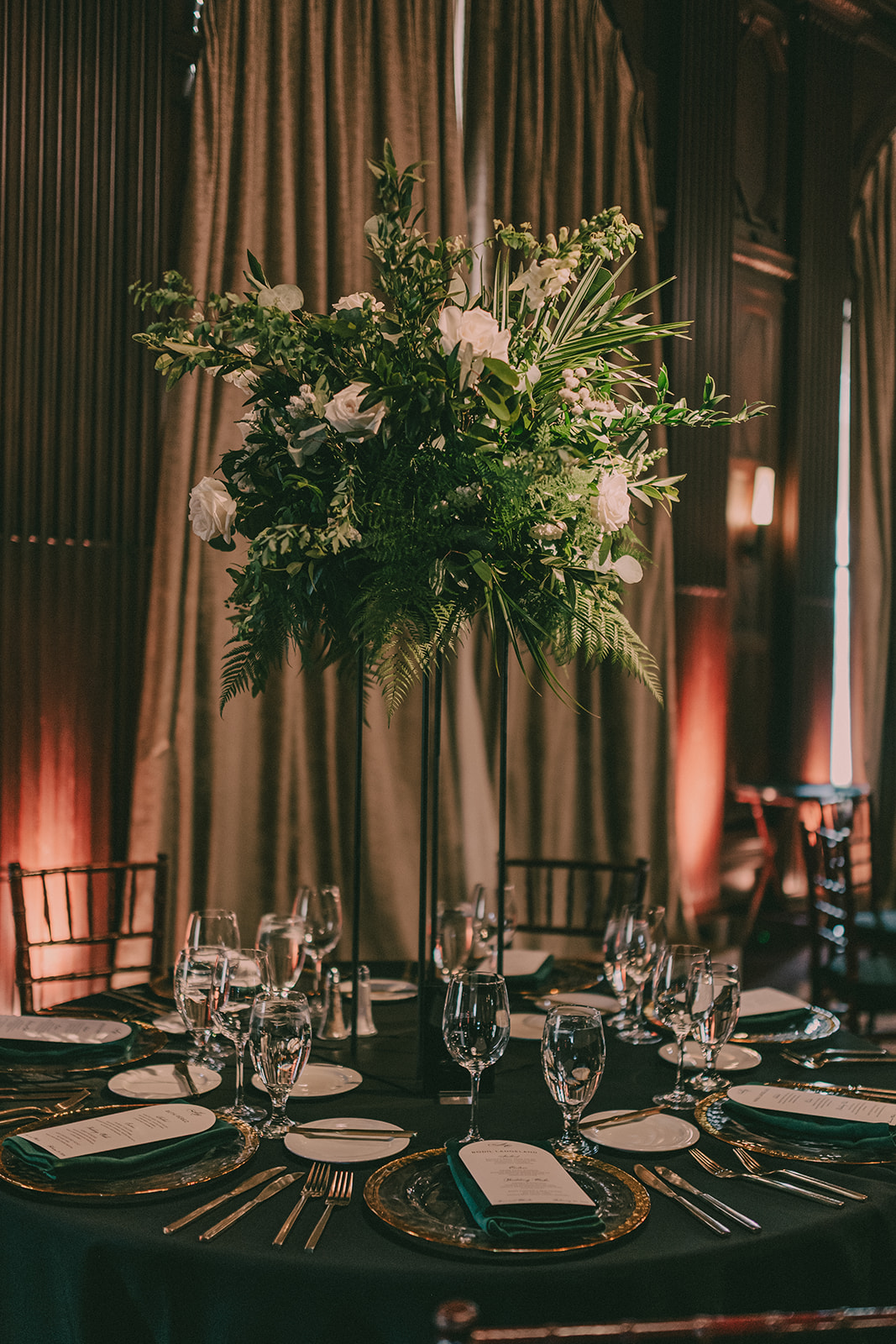 Tall green-and-white floral arrangement above a dark-green reception table.
