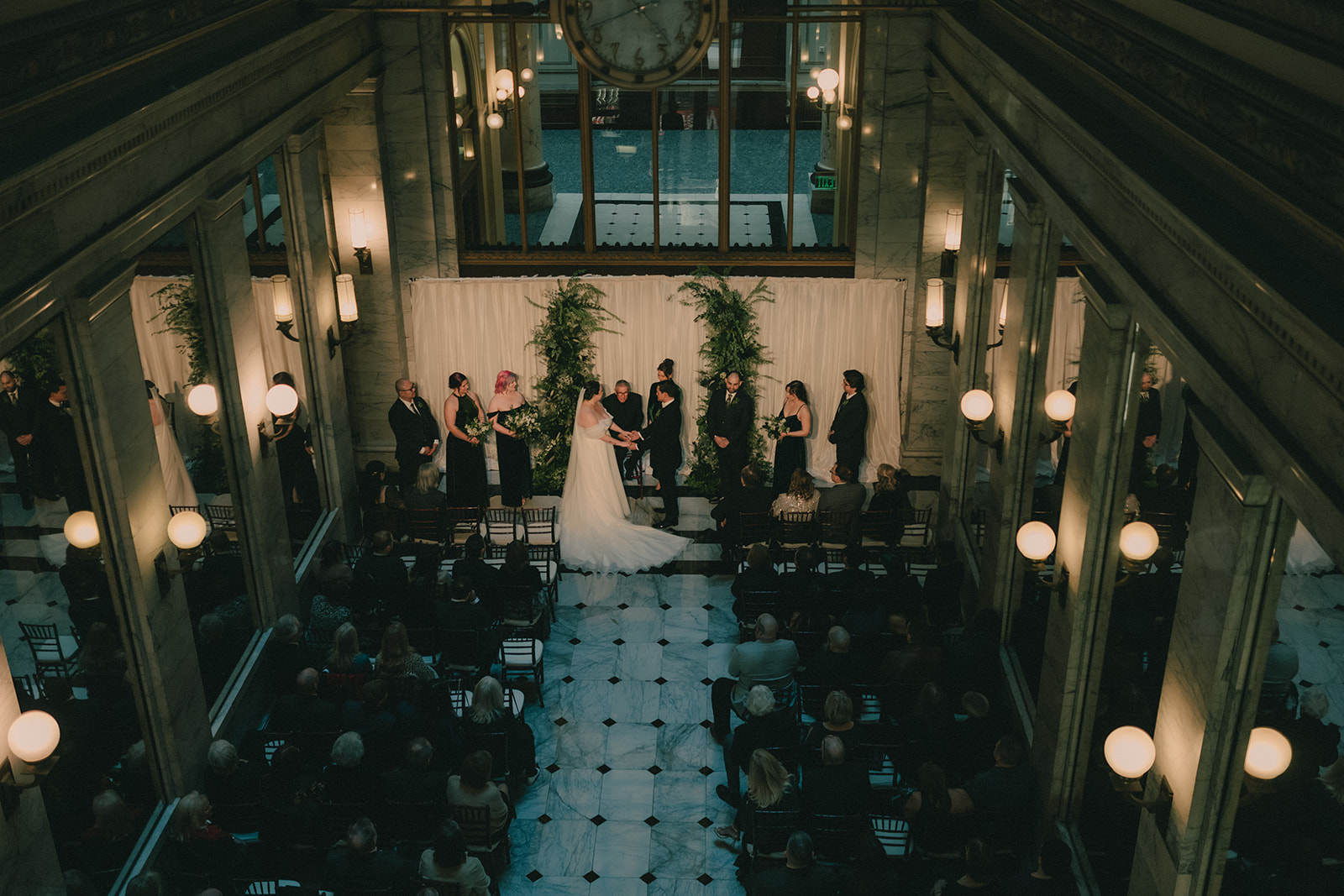 Wide overhead view of Anne and Charles exchanging vows in the marble lobby.
