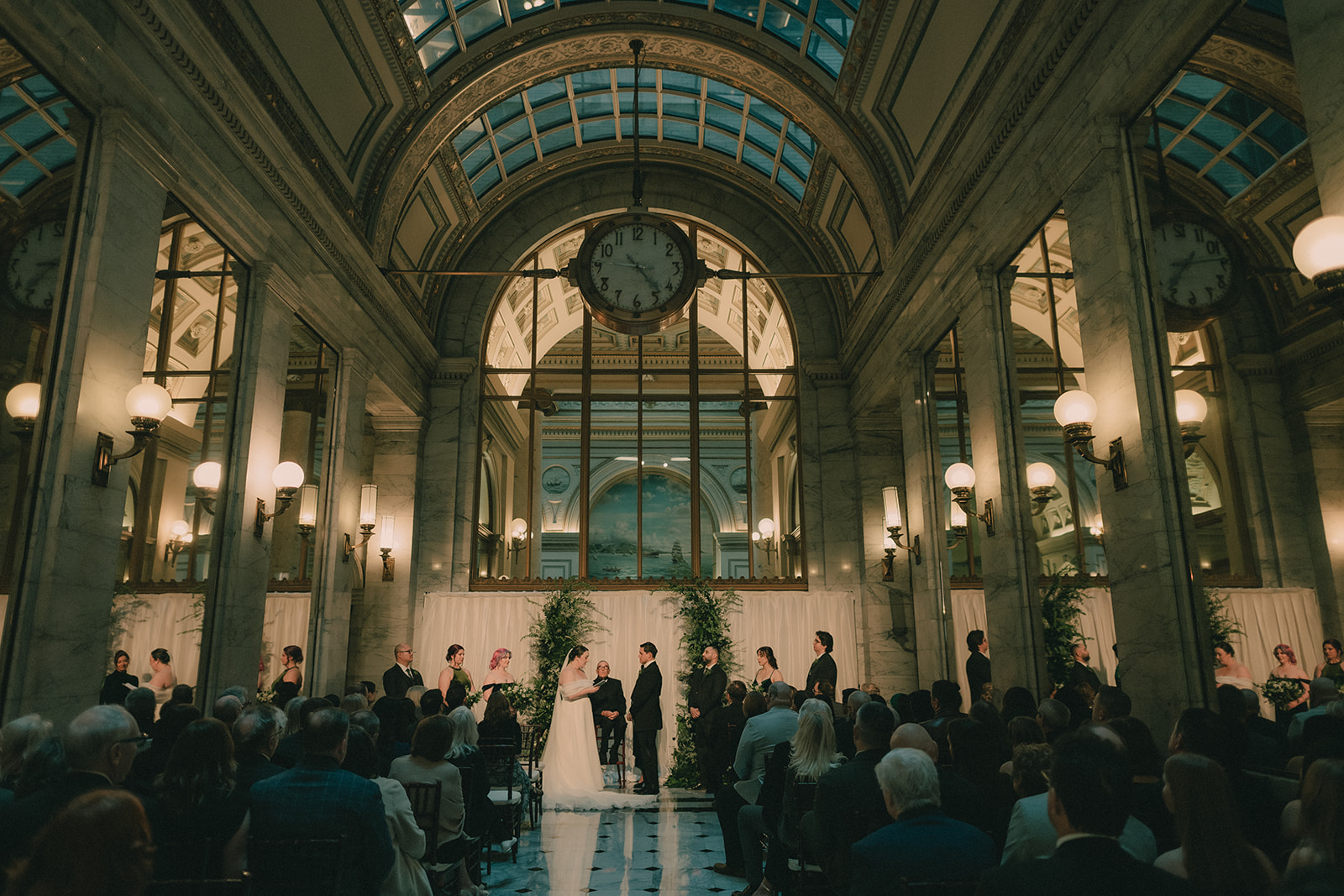 Wide ceremony view framed by marble columns, mirrors and the landmark clock.