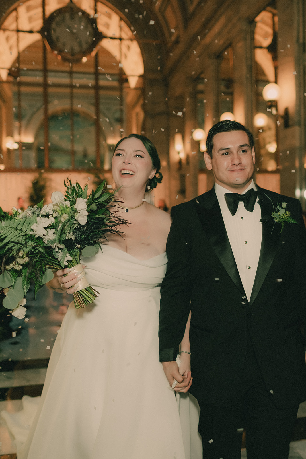 Anne and Charles smile beneath falling white confetti after their ceremony.