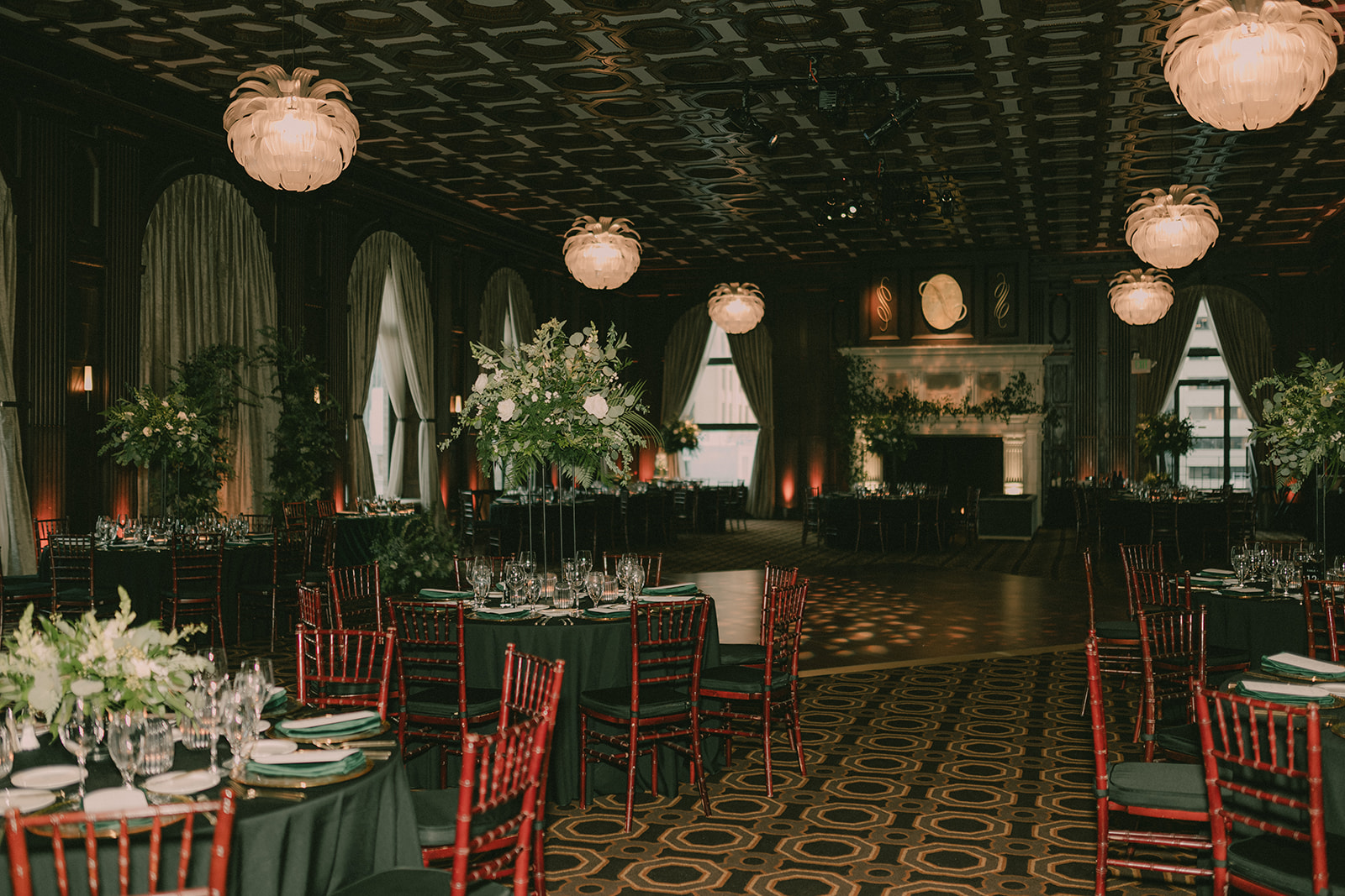 Wide view of the dark wood Julia Morgan Ballroom set with deep-green tables and tall florals.