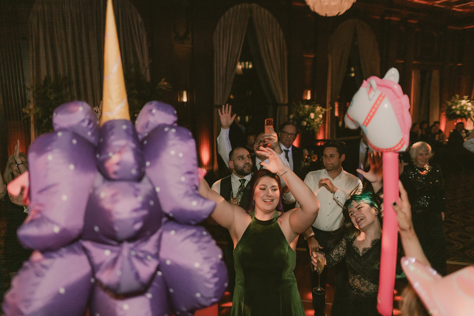 Wedding guests dance between pink pony props and colorful party lights.
