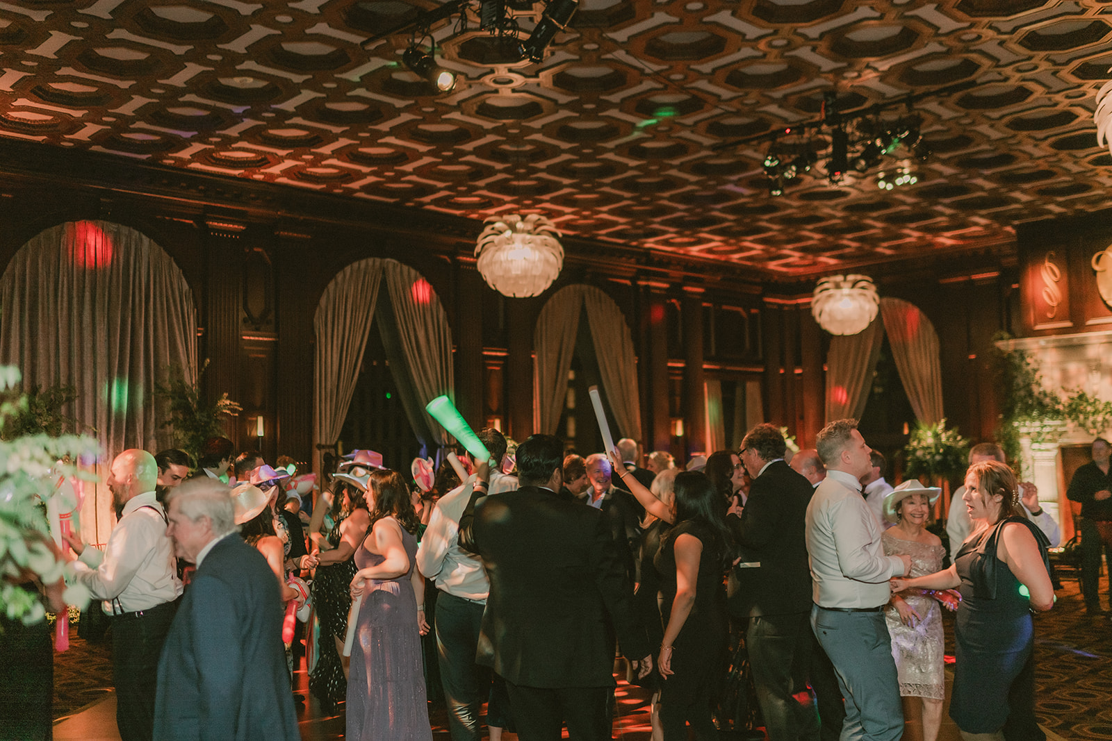 Wide view of a packed Julia Morgan Ballroom dance floor under warm red and green light.