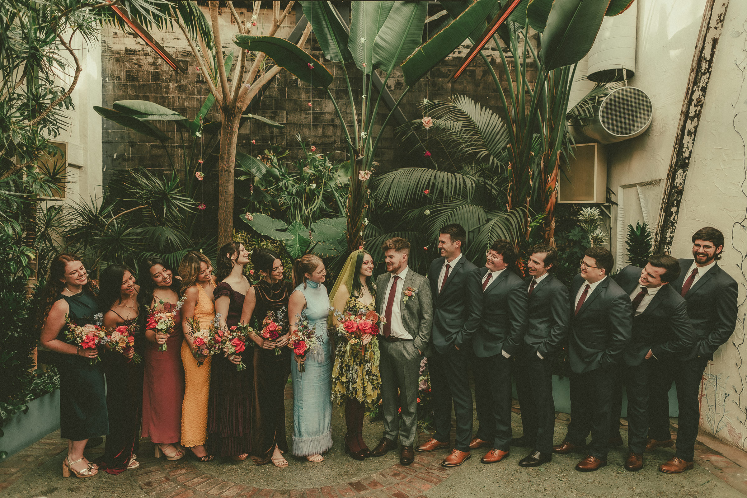 Lauren and Jack laughing with their full wedding party in a garden courtyard.