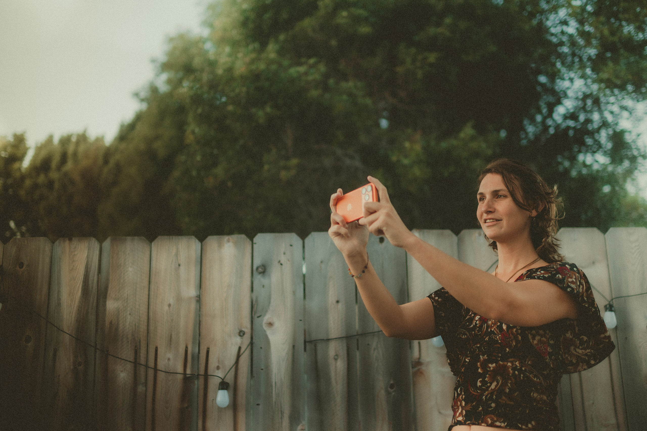 Faith filming with an iPhone beside a wooden fence.