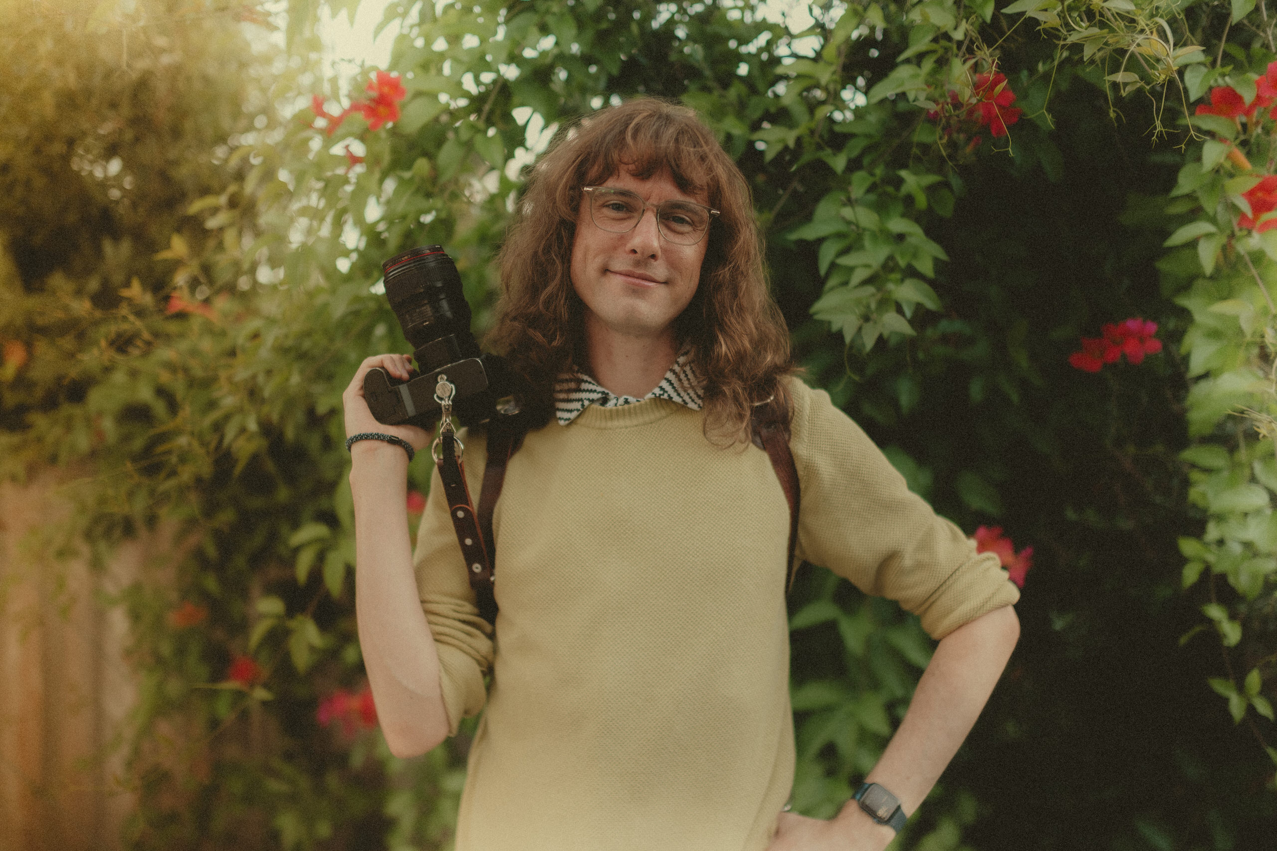 James resting a camera on their shoulder among greenery.
