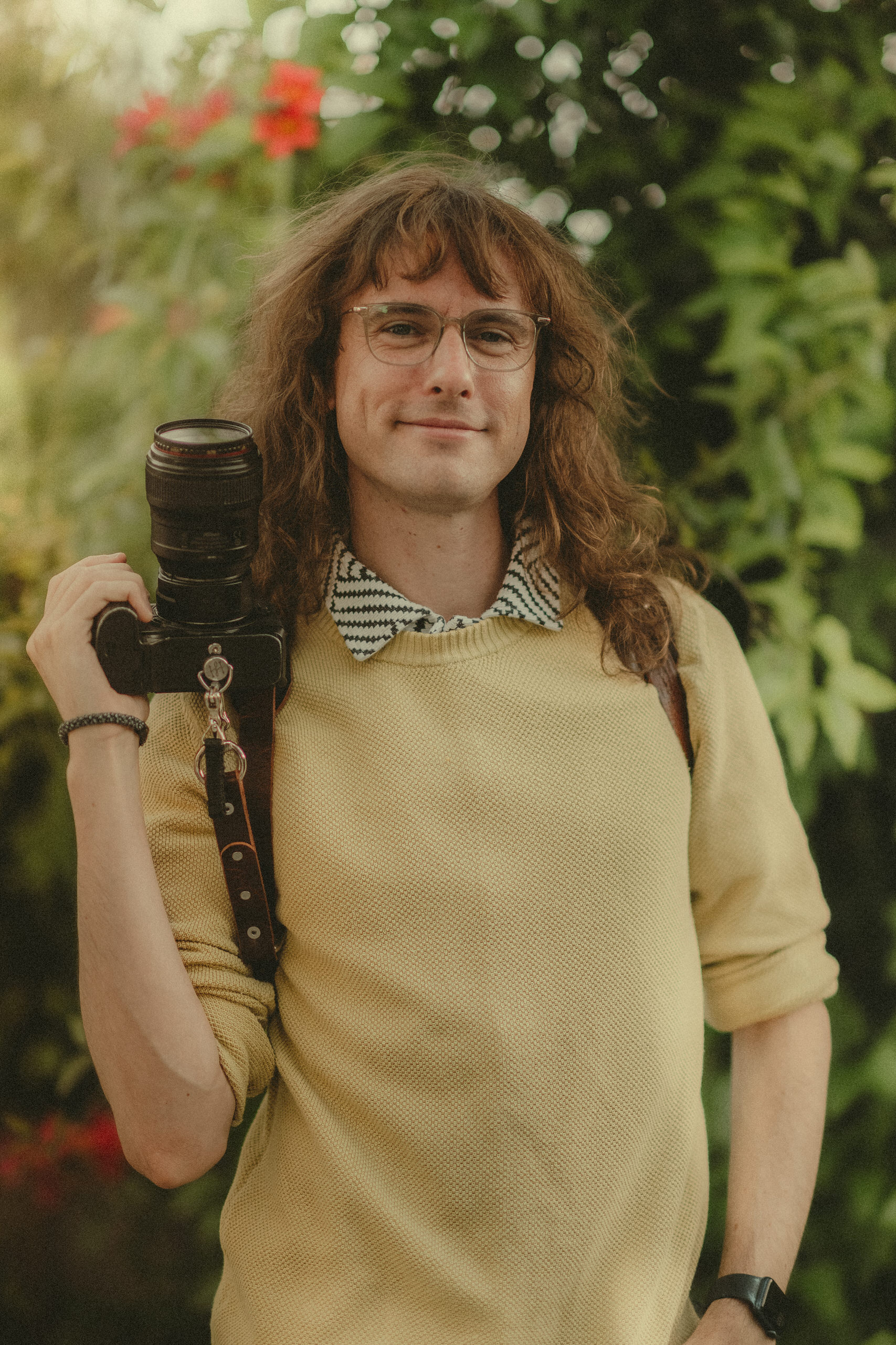 James Lester holding a camera in a relaxed outdoor portrait.