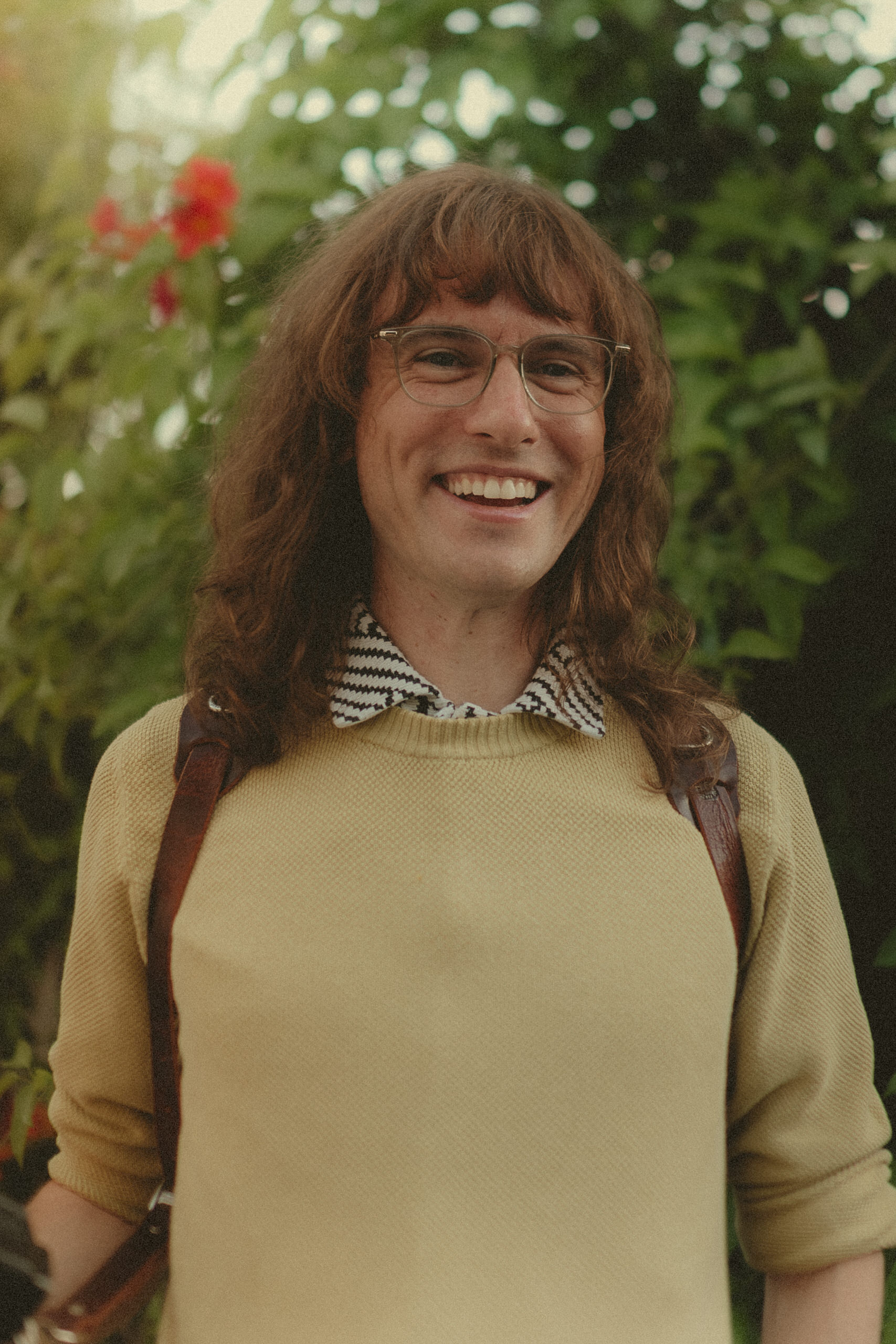 James Lester smiling in glasses and a sage sweater outdoors.