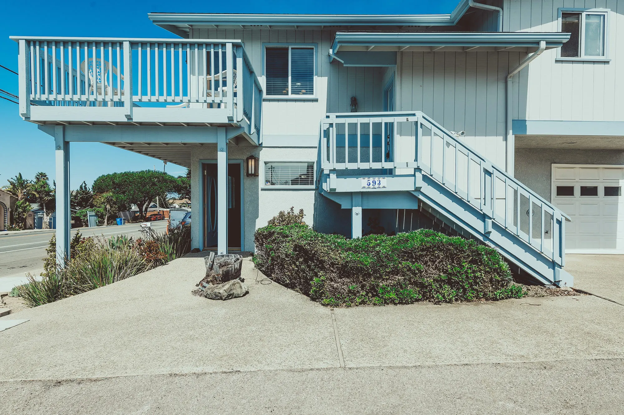 Ocean Avenue home with pale blue siding, a balcony, and sunlit exterior stairs