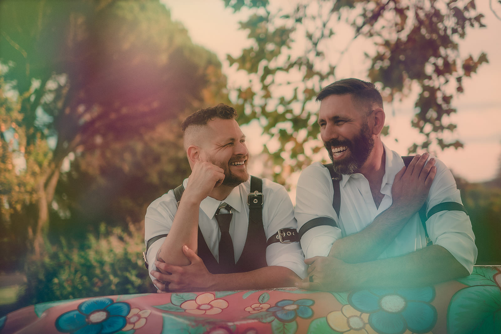 Sean and Stephan laughing on a flower-painted bench, framed by a soft green and pink light leak